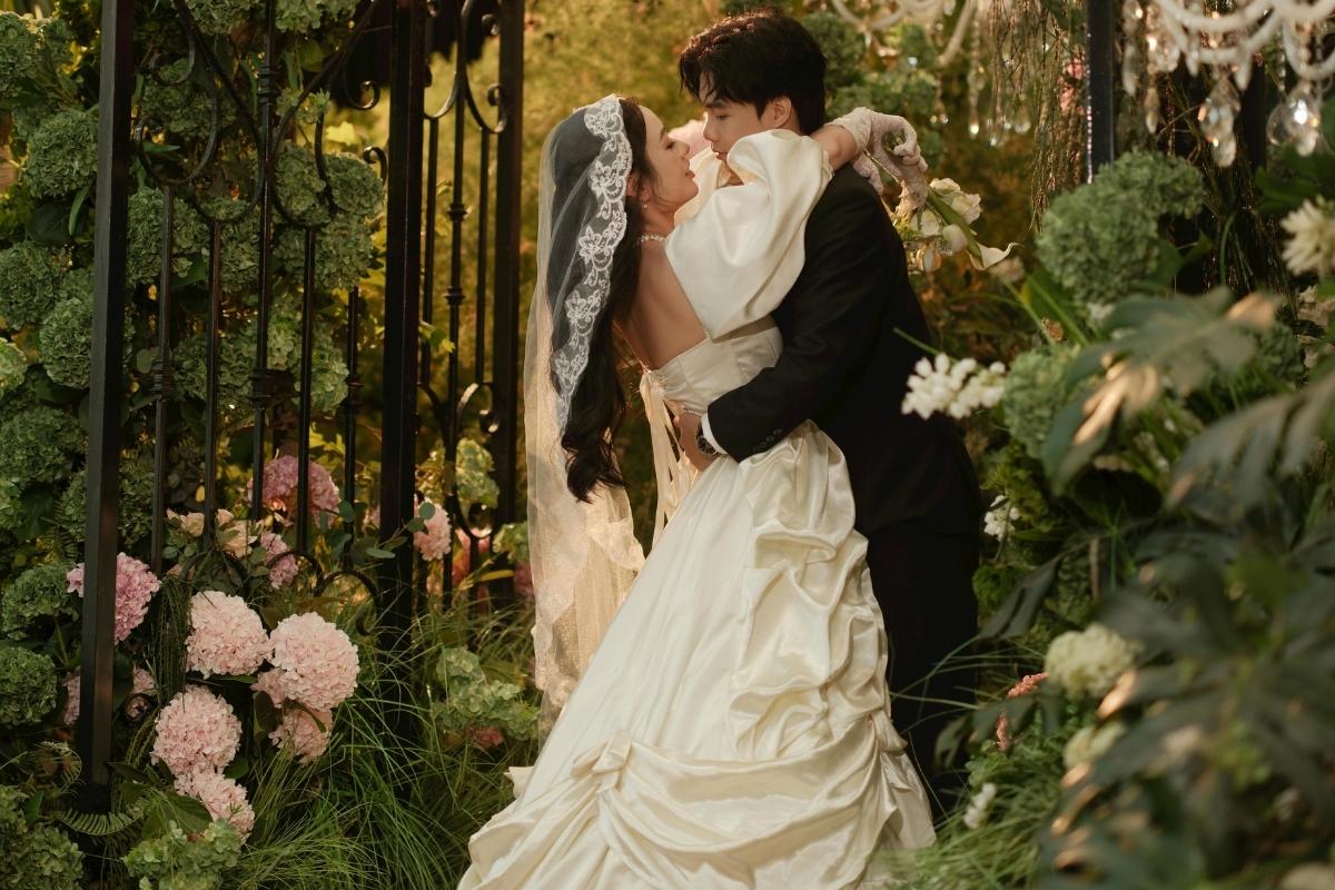 couple embracing in a romantic garden filled with green and pink flowers under warm lighting